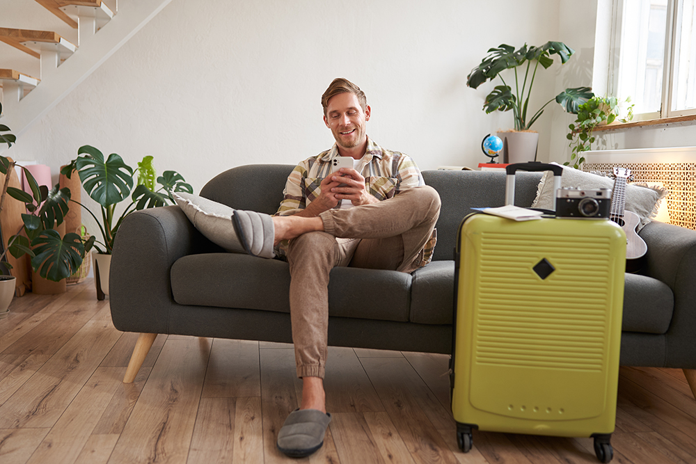 portrait young tourist man sofa with suitcase preparing holiday sitting with smartphone